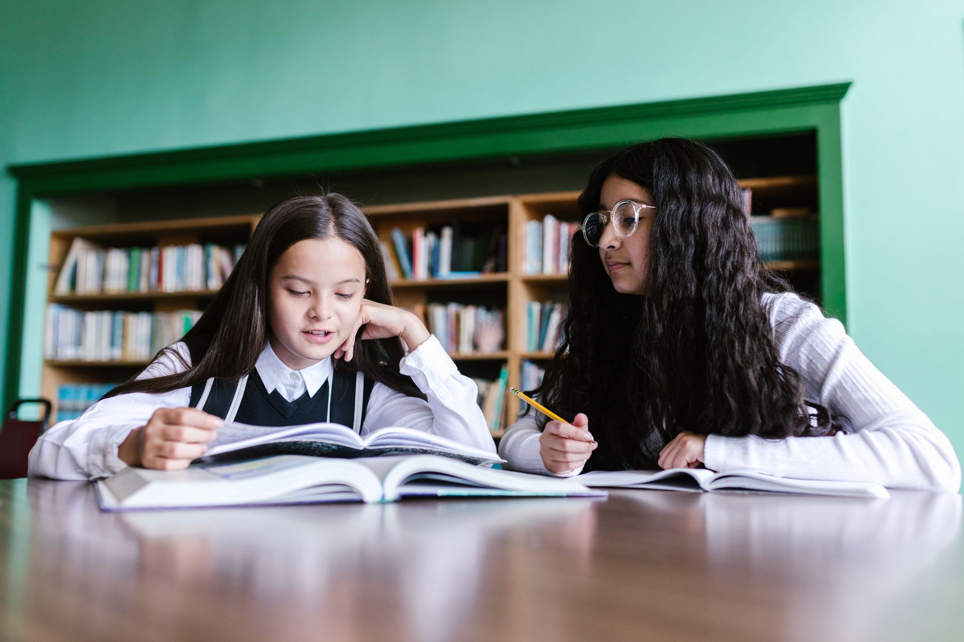 Dos alumnas estudian juntas con libros y cuadernos en una biblioteca